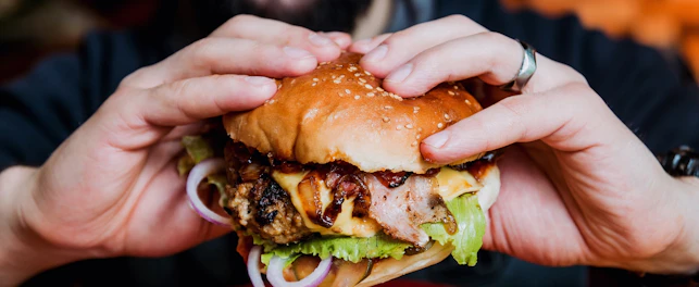Zbliżenie na cheeseburgera trzymanego w dłoniach przez mężczyznę.